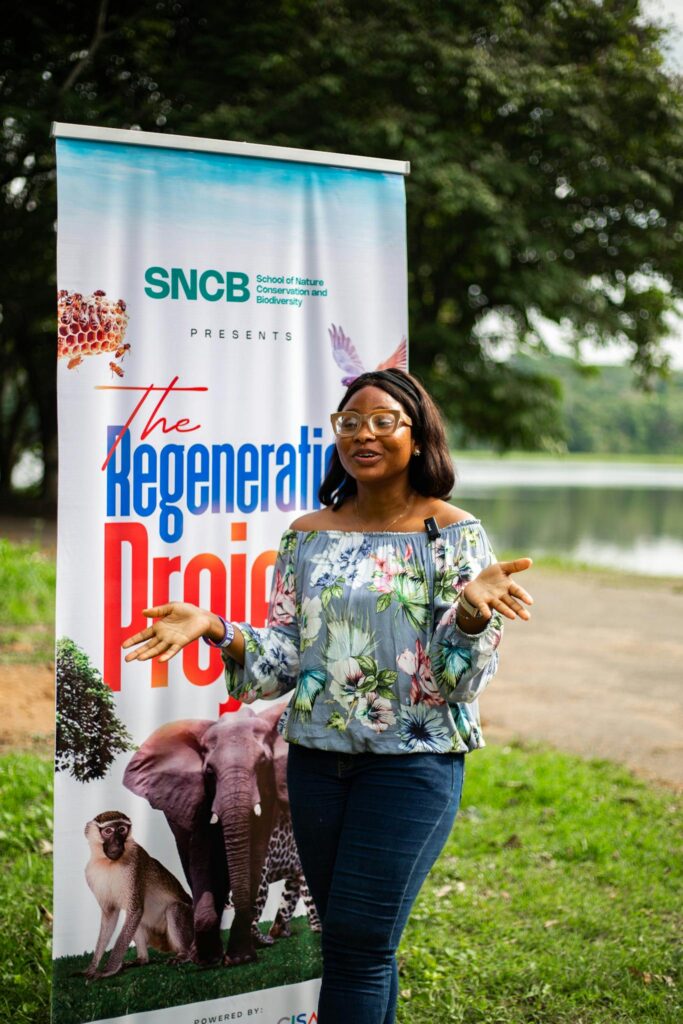 Young woman presenting at an outdoor environmental event beside a banner.